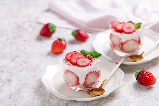 Strawberry tiramisu or trifle, dessert in a glass jar with fresh strawberry and mint leaves on a gray background