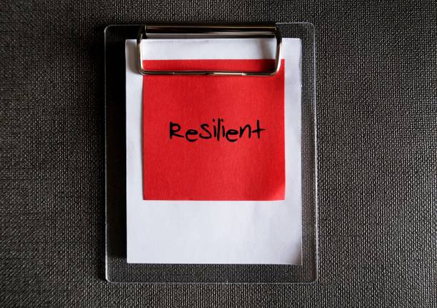 istock Red paper note clipping with clipboard on dark copy space background, with text written RESILIENT , concept of building ability to recover quickly from difficult conditions 1854308536