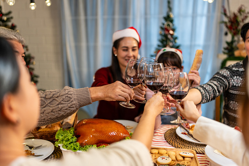 Asian lovely family celebrating Christmas party together in house. Attractive parents and relatives having dinner, toasting a glass of wine to celebrate holiday Thanksgiving, xmas eve on dining table
