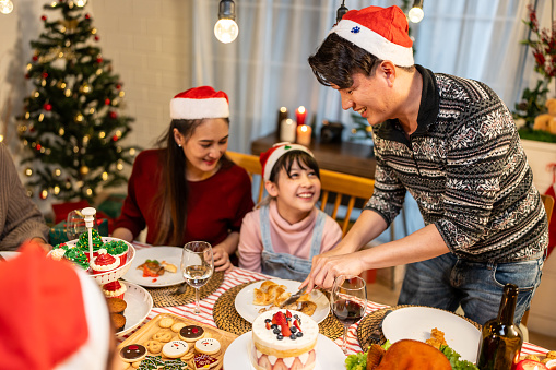 Asian lovely family celebrating Christmas party together in house. Attractive parents and relatives having dinner eating foods to celebrate holiday Thanksgiving, X-mas eve on dining table at home.