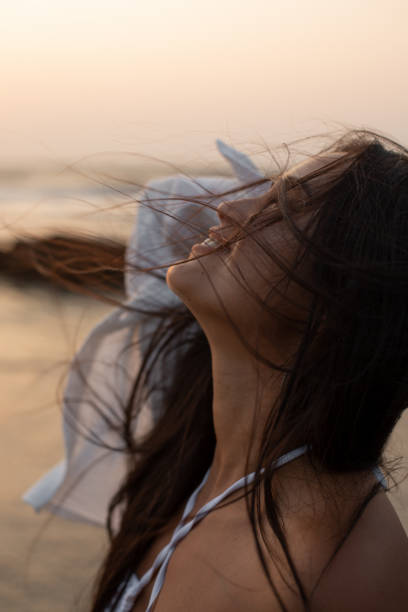 istock Playing with wind Young beautiful smiling brunette with loose long hair standing turned around seashore against sunset 1854322235