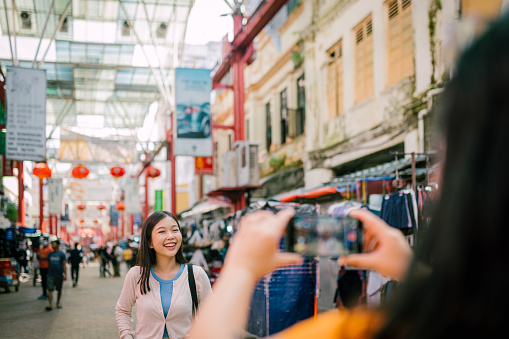 Happy asian woman posing while her friend taking a picture at local market. Gen Z lifestyle.