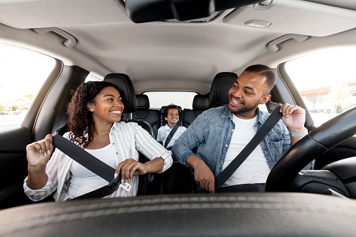 Safe Ride. Happy african american family young parents and son enjoying car journey together. Black mother looking at father while fasten seatbelt, getting ready for trip, family weekend
