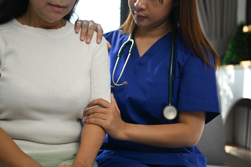 Positive female doctor touching shoulder of middle age patient for support, comfort and empathy