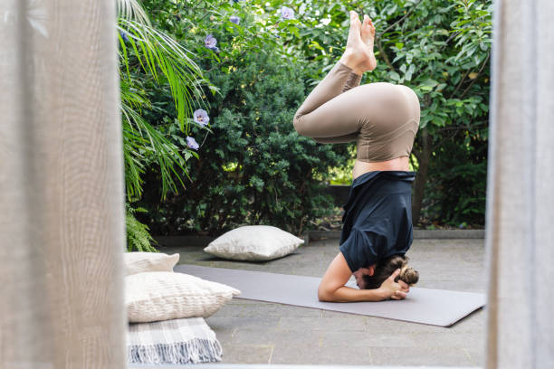 istock Young woman practicing yoga headstand position in a beautiful garden. 1854372714