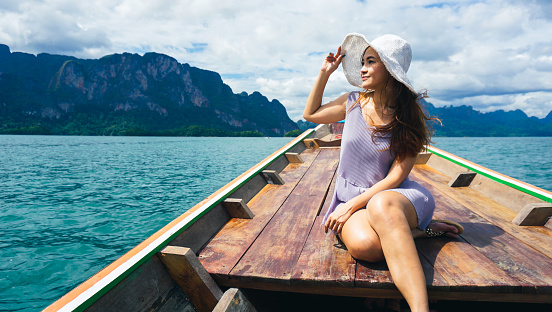 Beautiful woman sitting on long tail boat wearing straw hat at Ratchaprapha Dam or Chiao Lan Dam in Surat Thani Province, Thailand