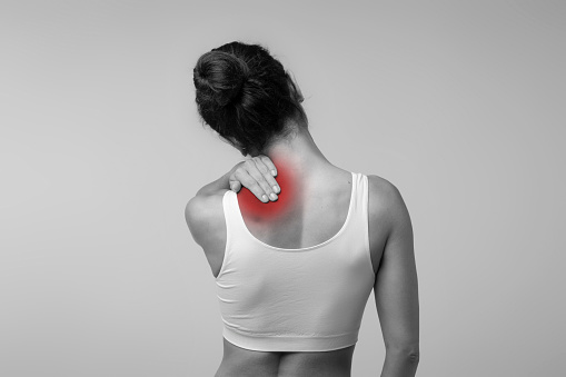 Neck pain muscle stress and strain concept. Stressed brunette woman massaging red sore neck, back view, black and white photo, studio background, copy space