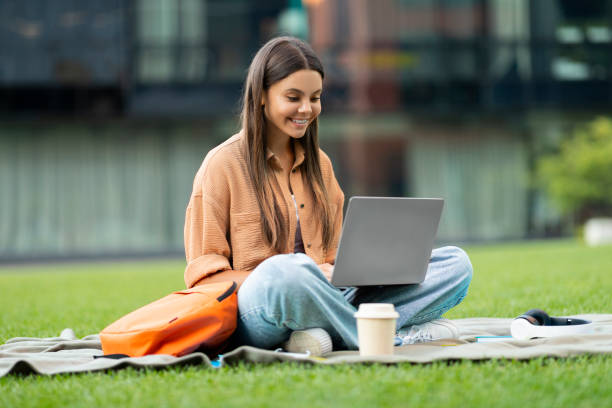 Cool pretty young woman college student using notebook at park
