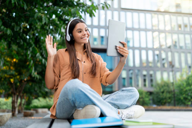 istock Woman student video calling on campus lawn, using digital tablet 1854409410