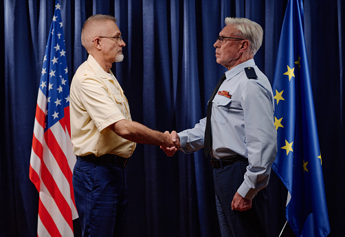 Politicians shaking hands to conclude a deal against american and european flags