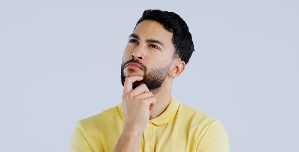 Handsome man wearing white t-shirt standing with hand on chin and looking away. Studio shot, grey background.