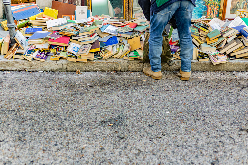 New and second-hand books scattered on the floor in a bookshop at El Rastro in Madrid. A passerby leans down to take a closer look.