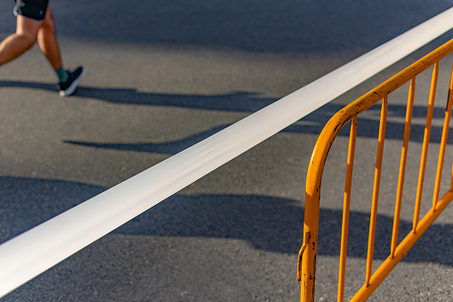 Madrid, Spain. Minimalist image with three distinctive elements defining a fun run through the central area of city streets and the traffic closures it involves. The barrier, the dividing plastic tape, and the runner's legs on the asphalt.