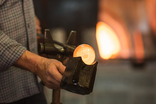 The worker makes a glass ornament in a glass smelter