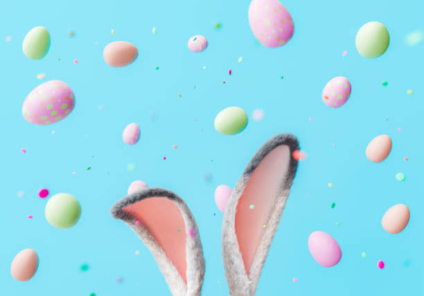 istock Bunny Ears with Floating Pastel Easter Eggs and Confetti on Blue Background 1854480546