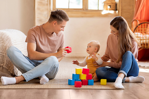 Caring Parents And Their Adorable Infant Son Playing With Toys At Home, Young Happy Mother And Father Spending Time With Cute Little Child, Having Fun Together In Living Room, Copy Space
