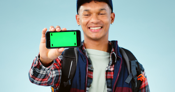 Hiking, green screen and man with a cellphone, smile and happiness on a blue studio background. Person, hiker and model with adventure, mockup space or smartphone with tracking markers or digital app