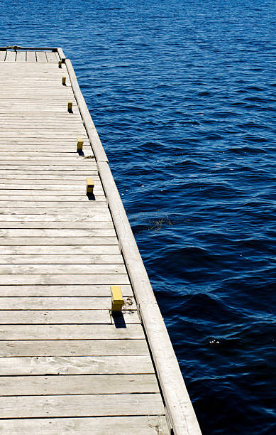 Wooden dock on blue water Part of grey wooden dock with metal cleats on blue water. bollard pier water lake stock pictures, royalty-free photos & images