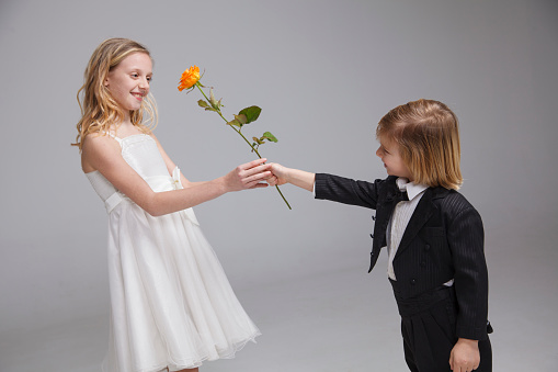 Boy giving his girl orange rose for birthday or valentine's day. Isolated on dark background.