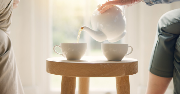 Pour, pot and hands with tea cup in morning, home and closeup on drink, steam and table. Hot, beverage and person with hospitality, service and drinking in the afternoon with guest in living room