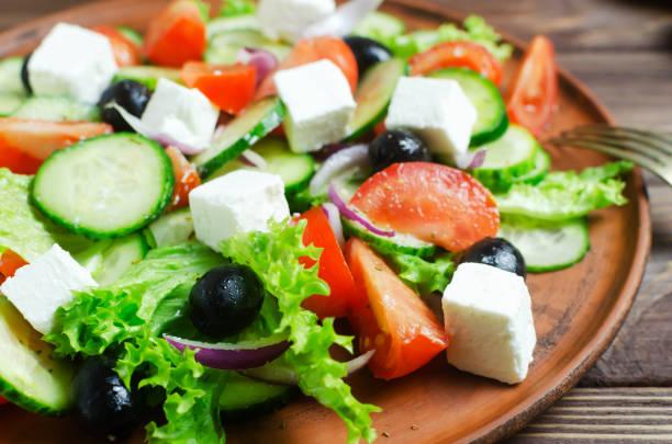 Classic Greek salad with cucumbers, tomatoes, red onion, feta cheese, lettuce and black olives on a wooden table. The concept of traditional dishes. Bossage. Simple ingredients. Top view. stock photo