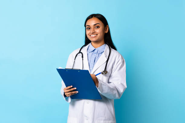 istock Indian Doctor Lady In Coat Posing With Clipboard, Blue Background 1854525831