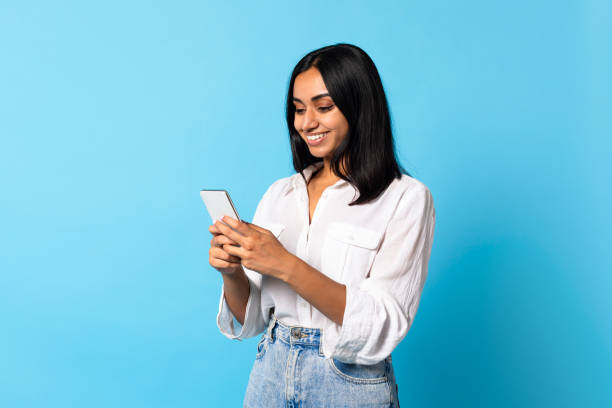 istock Indian woman scrolling via smartphone chatting online on blue background 1854528517