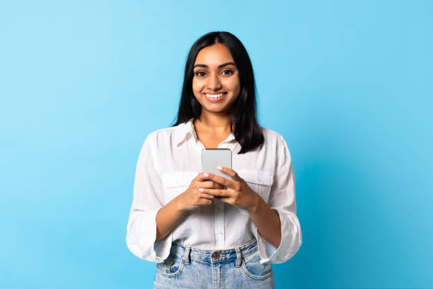 istock Indian lady texting on her smartphone on blue studio background. 1854528526