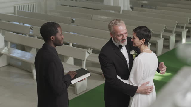 Mid-adult Couple Exchanging Wedding Rings and Cuddling by Altar
