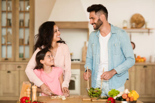 happy european parents teaching daughter how to cook, mother helping child girl chopping vegetables - two parent family indoors home interior domestic kitchen imagens e fotografias de stock
