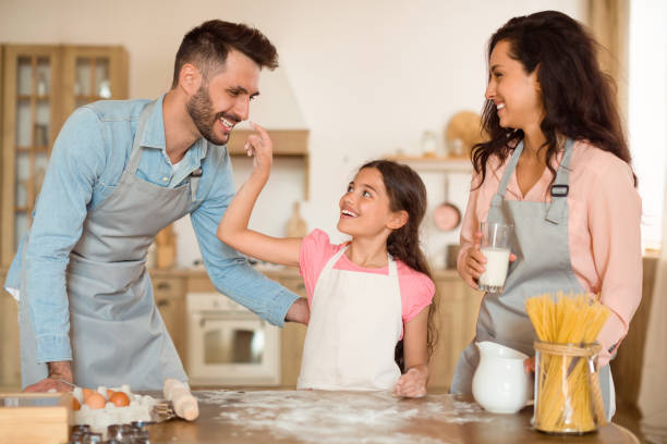 excited child girl playing with floor and dad while baking with parents together in kitchen - two parent family indoors home interior domestic kitchen imagens e fotografias de stock