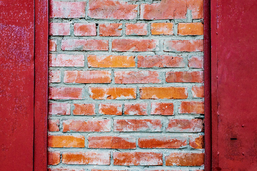 An old authentic brick wall with antique brickwork between metal red doors. Uneven defective brickwork. Background for the designer.