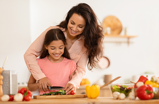 Happy Arab Mom And Daughter Cooking Salad Cutting Vegetables Together In Modern Kitchen Indoor. Young Mother Teaching Her Preteen Kid Girl To Cook, Spending Time Preparing Dinner. Family Nutrition