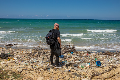 A handsome redhead male environmentalist volunteer cleaning up the plastic pollution from an Italian beach in Puglia