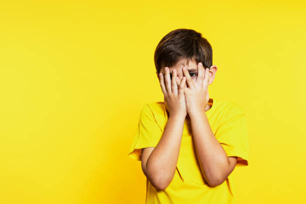 istock Curious Boy in Yellow Peeking Through Fingers Against a Yellow Backdrop 1854600088