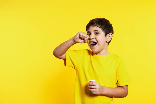 istock Happy Boy Eating Yogurt with Spoon on Vibrant Yellow Background 1854602218