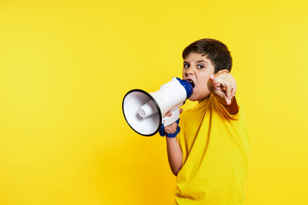 istock Passionate Young Boy Shouting Commands Through Megaphone on Yellow 1854607260