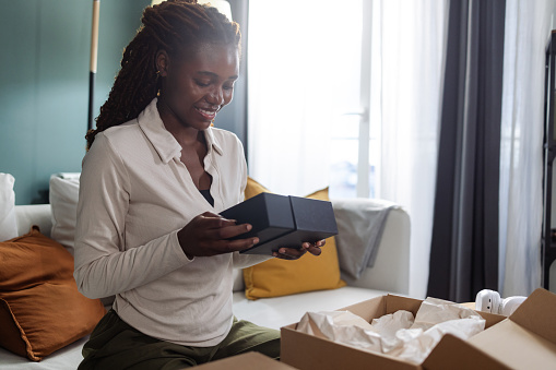 A Young African American woman cheerfully unboxing her online purchase that has just arrived.