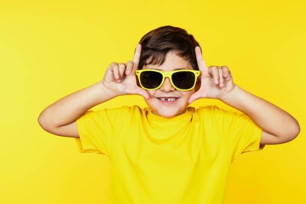 istock Happy Boy with Sunglasses Making Hand Signs on Yellow Background 1854615053