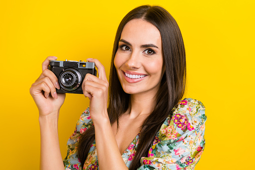 Portrait of lovely positive woman with long hairstyle wear stylish dress hold camera make photo isolated on yellow color background.