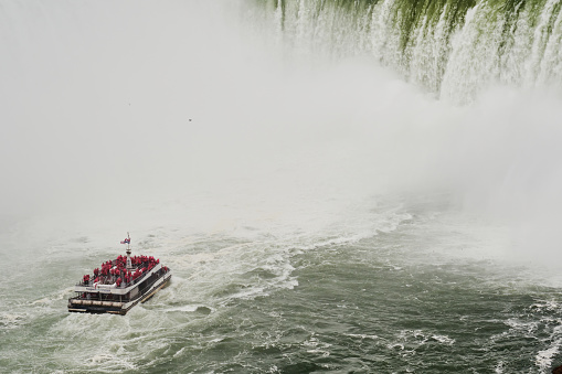 Niagara Falls, Ontario, Canada; 10th of October 2023: One of the cruise boat that work in Niagara River heading to the water fall with a group of tourist wearing pink raincoats in it in a rainy and misty morning of autumn