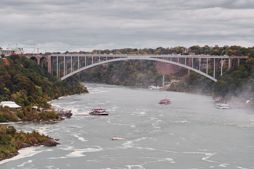 Niagara Falls, Ontario, Canada. A view of the Niagara River, two boats and the Rainbow International Bridge that link Canada and United States in a cloudy day.