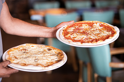 Waiter carrying two different plates with a tasty pizza. Photo with two pizza. Pizza with mushrooms and pizza with salami. Italian food. Italian restaurant.
