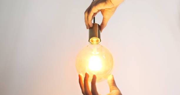 istock Male hands screw a light bulb into a socket. Close-up. Yellow bright light, the light bulb on the wire lights up. 1854654828
