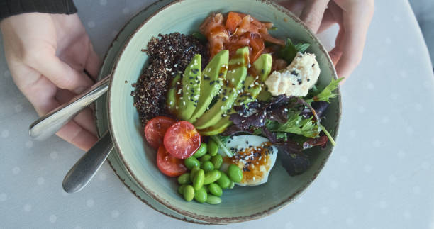 istock Bowl plate, top view, female hands rotate the dish. Fresh salmon, avocado, boiled egg, soft cheese, tomato, green beans. Appetizing dish in the restaurant. 1854654851