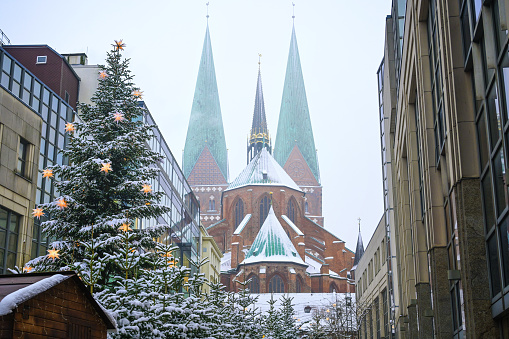 Fir trees with shining stars at the Christmas market behind the Marienkirche (meaning St. Mary church) on a snowy winter day in Lubeck, Germany, copy space, selected focus