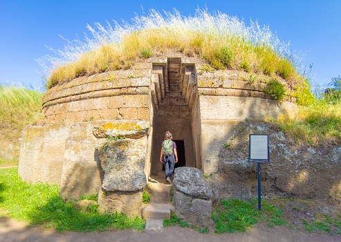 Cerveteri, Italy - 8 May 2022 - Beside Rome, Cerveteri is one of most important Etruscan cities with archeological necropolis namen Necropoli della Banditaccia, Via degli Inferi path and waterfalls. Here in particular a view of tomb's exterior open door with girl tourist