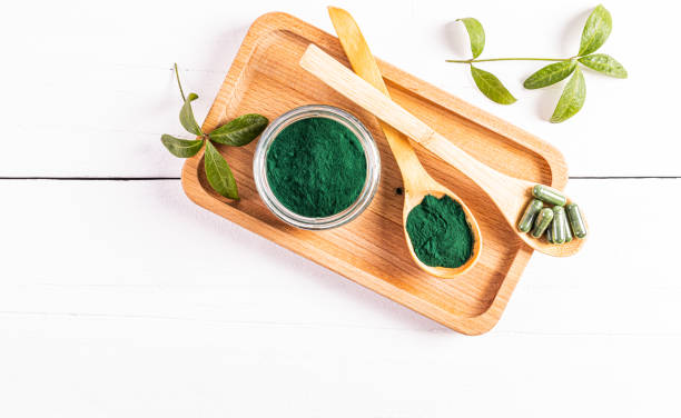 A glass jar of green organic spirulina powder and two wooden spoons filled with powder and capsules on a wooden tray. Top view. Detox A glass jar of green organic spirulina powder and two wooden spoons filled with powder and capsules on a wooden tray. Top view. Detox. chlorella stock pictures, royalty-free photos & images
