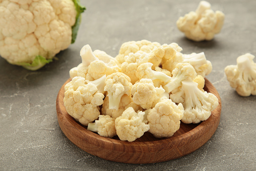 Wooden bowl of cauliflower on grey background, top view