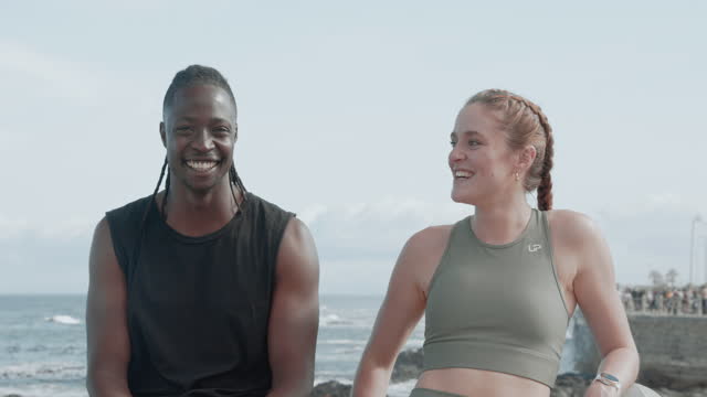 Happy people, friends and beach for fitness, training or workout together by the ocean coast. Man and woman laughing and smile for funny joke on break after cardio exercise in health and wellness